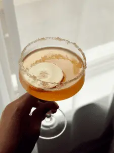 golden brown cocktail in coupe glass in front of a window with soft lighting from sheer curtains