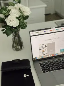 mackbook sitting on a white counter top with an arrangement of white roses behind it