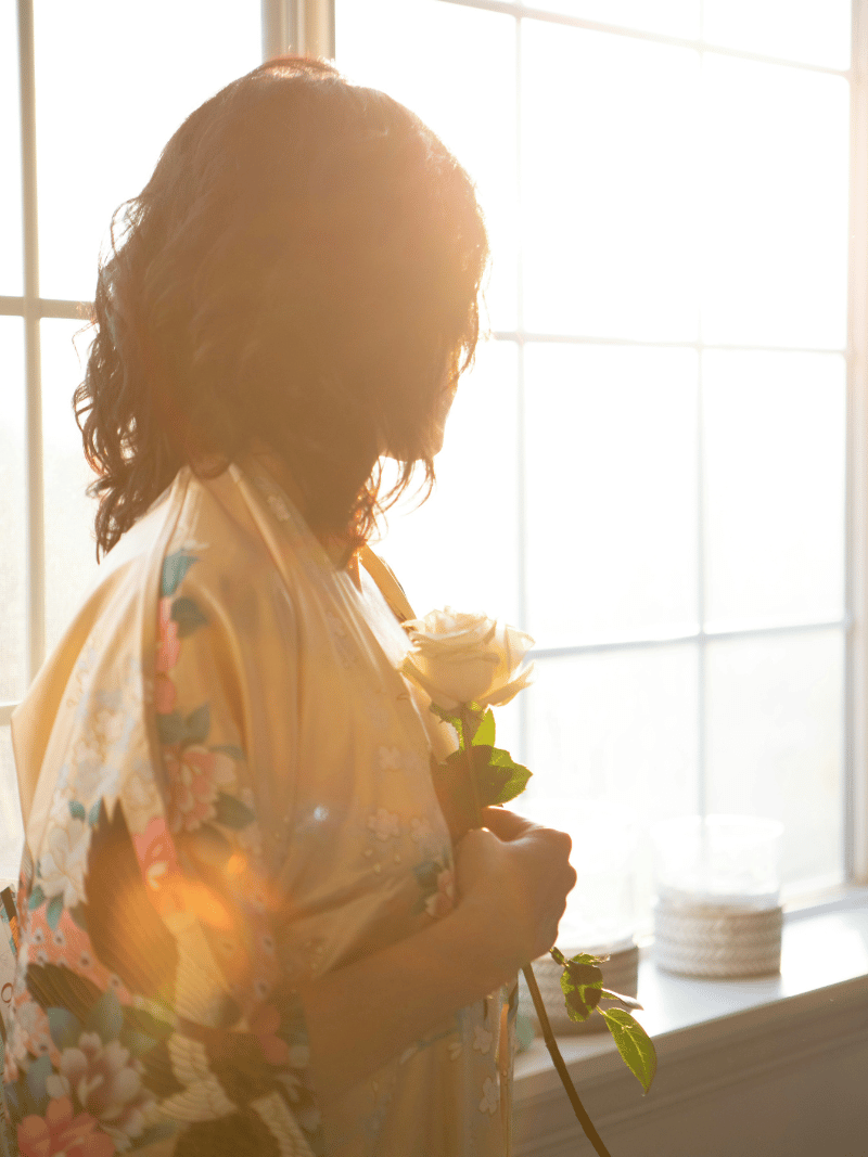 woman looking out window holding a white rose