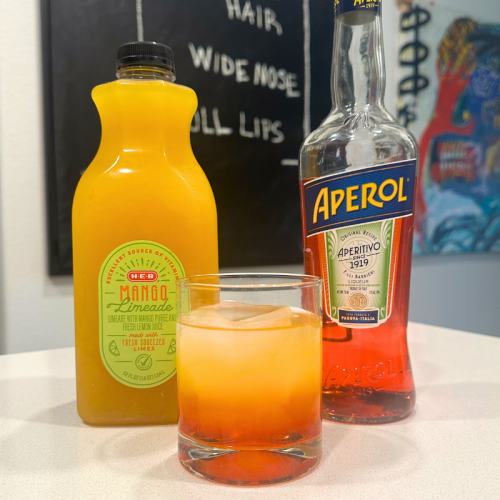 orange and red mango lime aperol sunrise in cocktail glass on white counter top