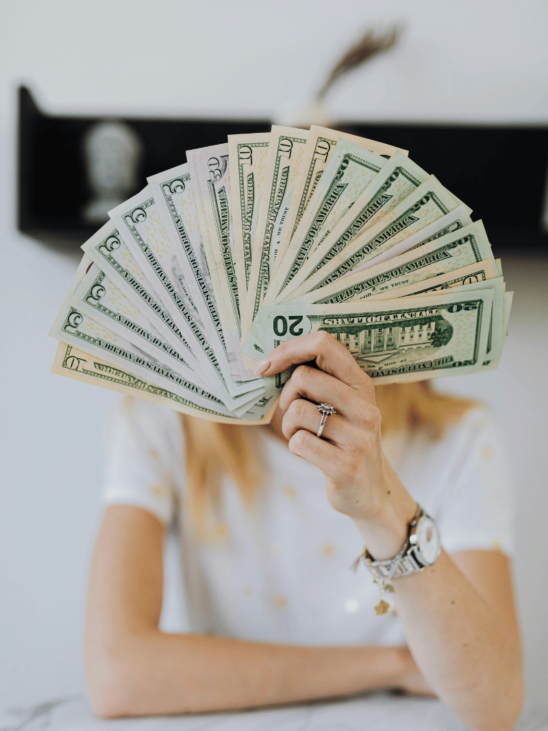 woman holding a fan of twenty dollar bills in front of her face