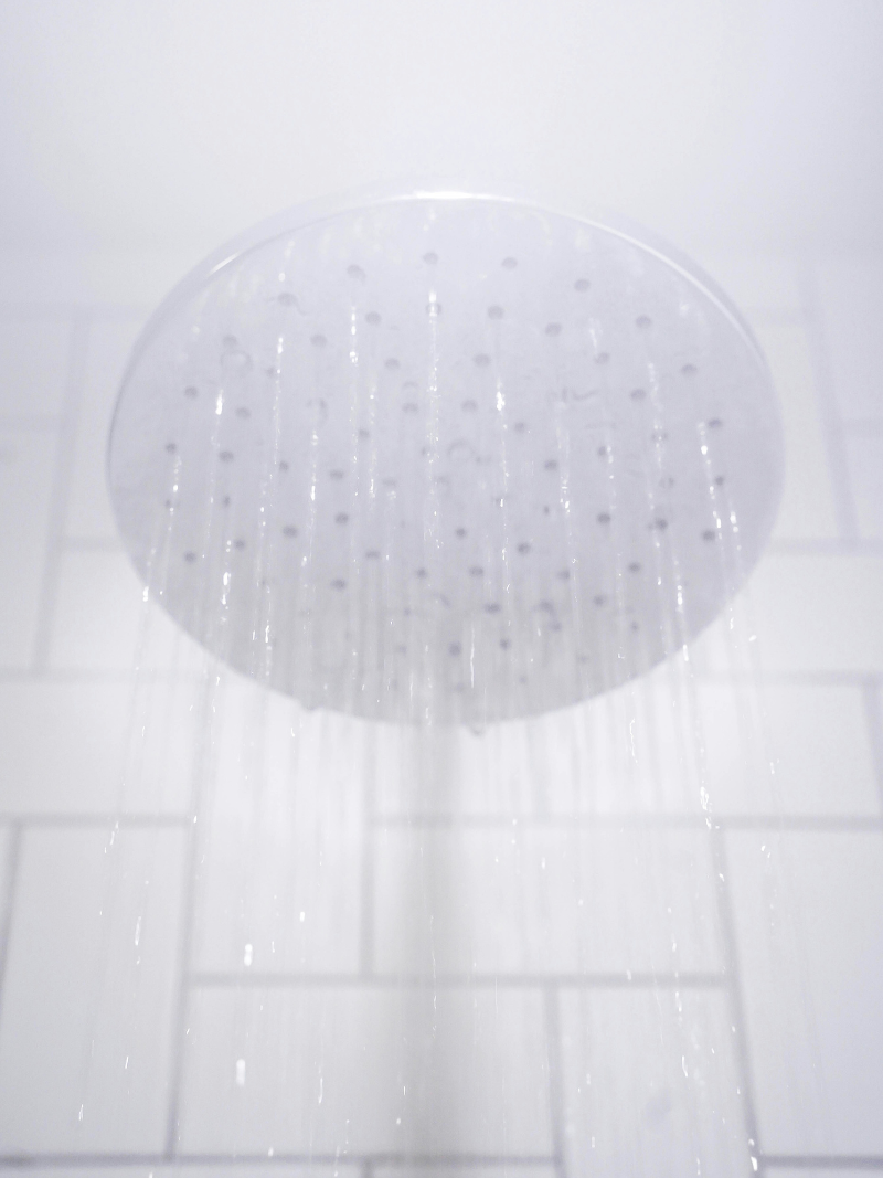 chrome shower head spaying water in a white tiled shower