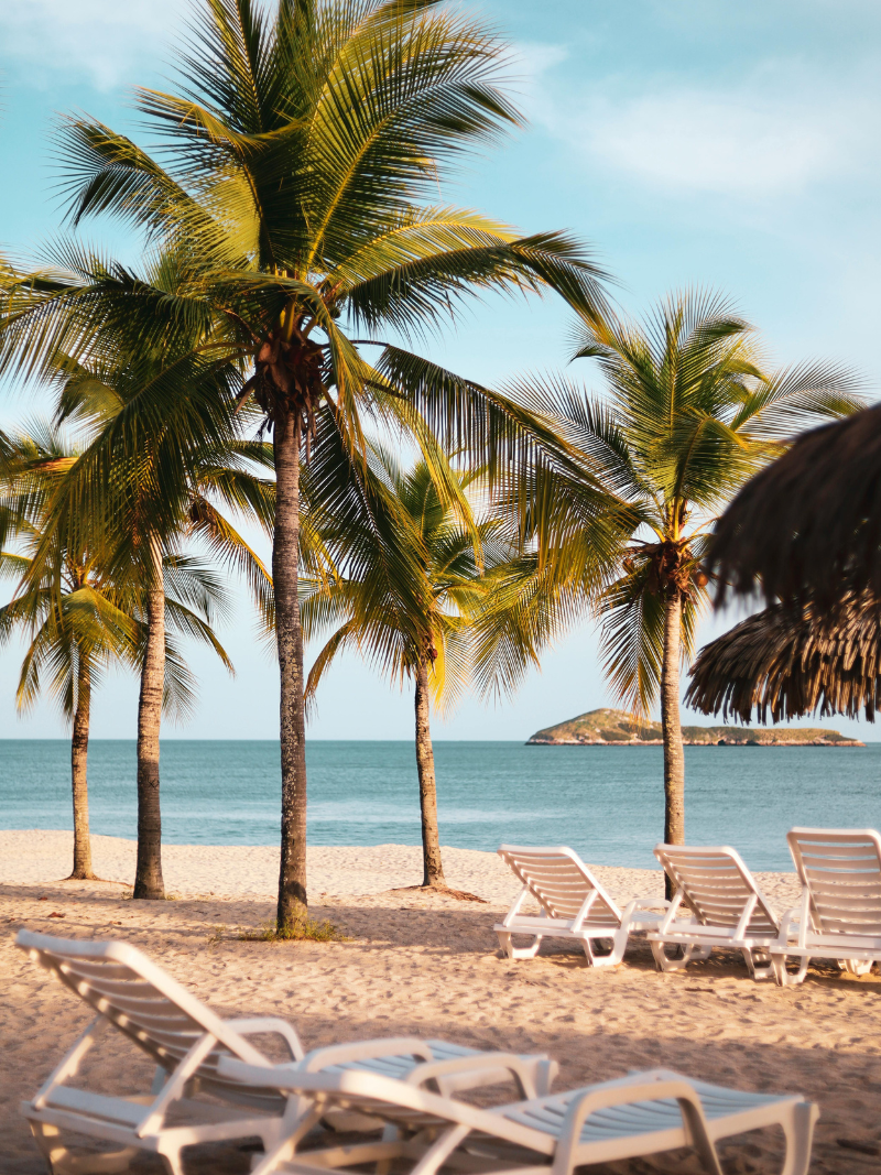 white beach chairs on a pristine beach - hacks for traveling on a budget