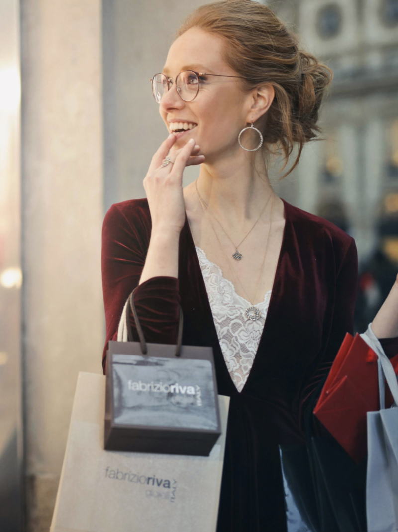 woman looking longingly in a store window holding shopping bags
